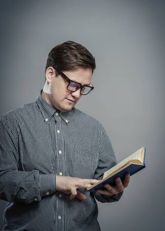 Portrait of young man in glasses reading isolated over grey backgroundの写真素材