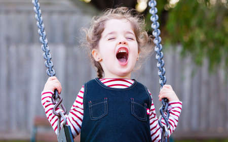 A young girl has fun swinging in a playgroundの写真素材