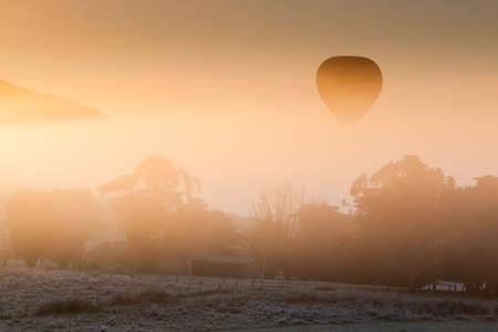 A hot air balloon rises thru the fog just as the sun rises on a cold winterの写真素材