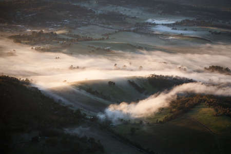 Fog rolls across hills at sunrise in the Yarra Valley in Victoria, Australiaの写真素材