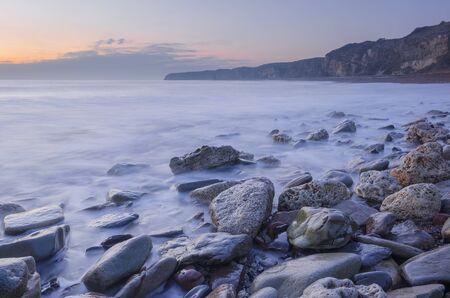 calm sea on a rocky beach before sunriseの写真素材