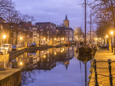 Dutch old city Schiedam landscape during calm weather with reflections in a canal, old barges and church towerの写真素材