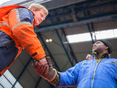 Smiling Europian deck officer wearing orange overall and working gloves friendly shakes a hand of...
