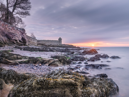 Colorful sunrise over rocky beach and calm sea with old medieval watch tower near Kirkcaldy Scotlandの写真素材