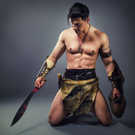 Muscular  man in the image of ancient warrior on a gray background