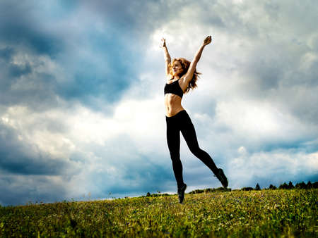 The red-haired girl is engaged in sports exercises on the field under the clouds in an unexpected ray of sunshineの写真素材