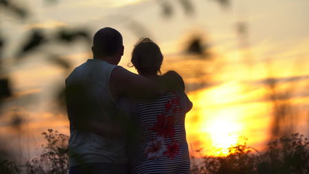 Man and woman embracing each other looking at the sunset. The woman put her head on the man's shoulderの写真素材