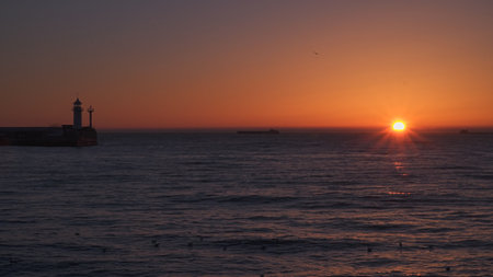 Sunrise at sea. Ships and a lighthouse can be seen on the horizon.の写真素材