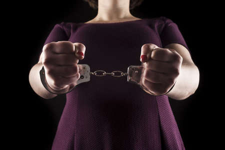 submissive woman wearing a purple dress in metal handcuffs on black background