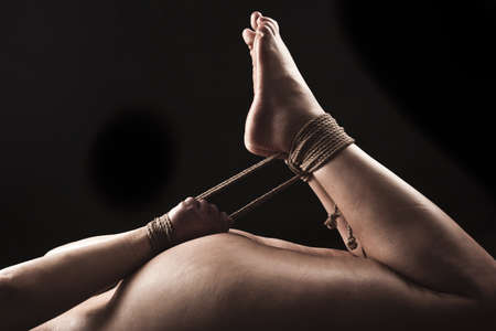 Submissive woman in hog tie bondage position on black background / BDSM theme