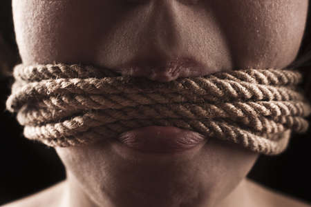 submissive girl gagged with rope on a black backgroundの写真素材
