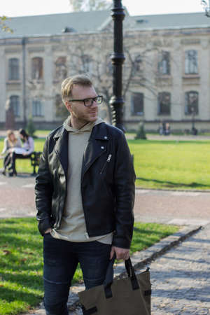 Smart smiling guy in casual clothes looking to the left, walks next to the university, a successful...