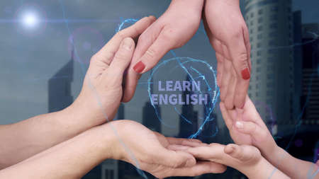 Mens, womens and childrens hands show a hologram Learn English. The family holds a magical inscription on the background of a modern cityの写真素材
