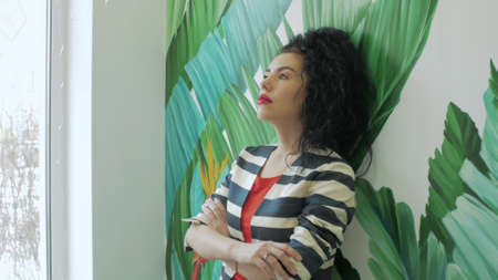 Dreamy woman against the background of colored green leaves and a window. Attractive girl on the...