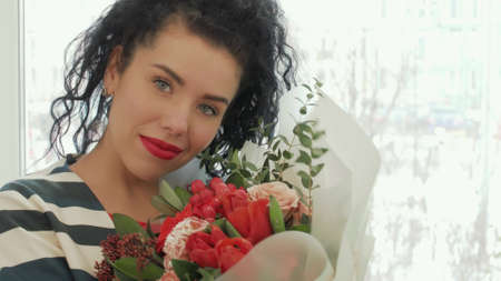 Beautiful curly woman with a gorgeous bouquet near the window. An attractive girl with a lovely...