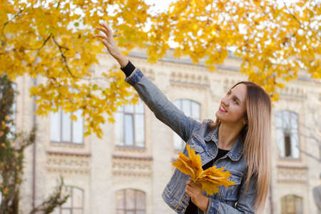 Warm lifestyle colorful photo of a cute woman. Lady holds in her hand yellow leaves. Sunny autumn...