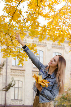 Warm lifestyle colorful photo of a cute smiling woman. Lady holds in her hand yellow leaves. Sunny autumn conceptの写真素材