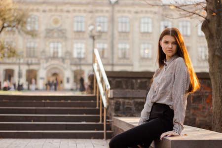 A student sits near the steps leading to the university. Young woman in autumn park. Concept of...