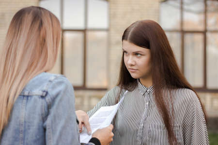 Unhappy girl is standing near the university and look at the adult with paper. Sisters are studying the contract for admission. Elder carefully explains younger test resultsの写真素材