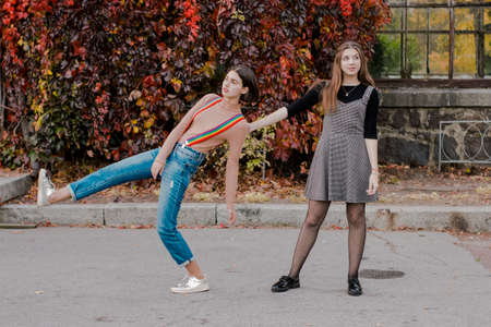 Two beautiful students walking in the autumn park. Girls have fun outdoor