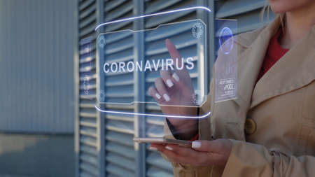 Unrecognizable businesswoman interacts HUD hologram with text Coronavirus. Woman in the coat uses...