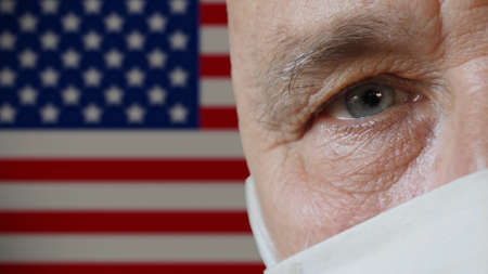 Half face of elderly man in protective mask close-up on copy space background of USA flag. Health...