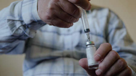 An elderly male hands hold a syringe and pour the substance into the vaccine bottle. Health and medical concept of the elderlyの写真素材
