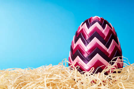Beautiful easter egg in hay on blue background. Copy space.の写真素材