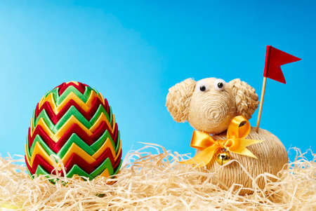 Easter egg and easter lamb with red flag and yellow bow on the blue background.