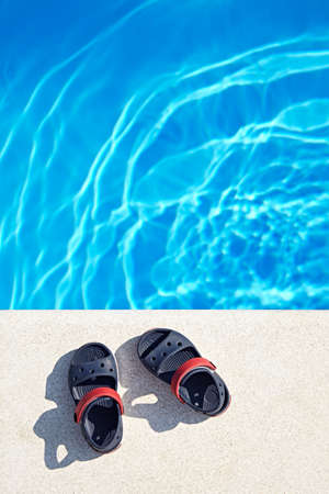 Pair of baby sandals at the swimming pool at sunny day. Copy space.