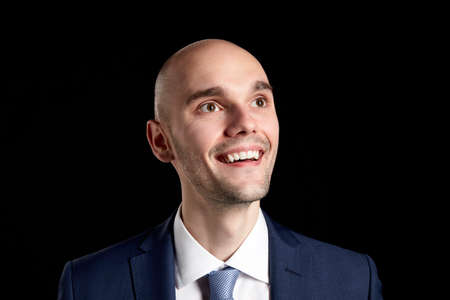 Portrait of young smiling man looking up. Studio shot on black background. 