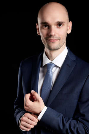 Young man fixing sleeve his suit. Close up portrait on black background.