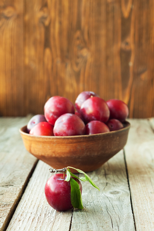 Vintage ceramic bowl with plums on rustic wooden tableの写真素材