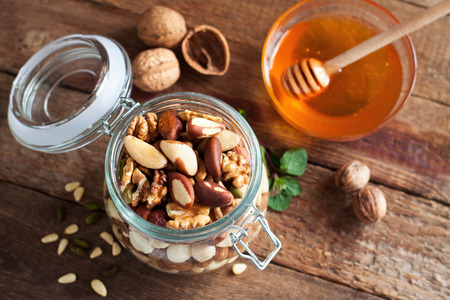 Assortment of nuts in a glass jar and honey on rustic wooden table. Top viewの写真素材
