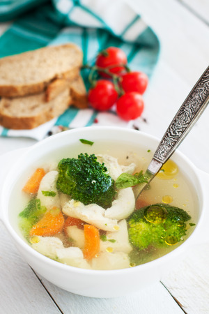 Chicken detox soup with carrots, broccoli, celery, onion and herbs on white wooden tableの写真素材
