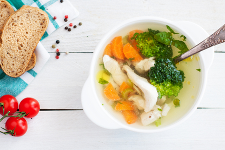Chicken detox soup with carrots, broccoli, celery, onion and herbs on white wooden tableの写真素材