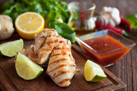 Barbecued chicken fillet with spicy sauce, served with fresh basil, lime and lemon on wooden cutting boardの写真素材