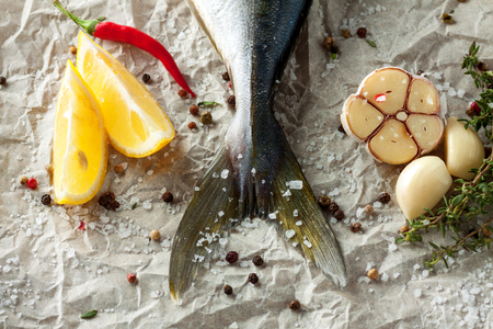 Top view of fresh tuna tail with chili pepper, lemon, garlic, herbs and spices on baking paperの写真素材