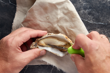 View of male hands shucking fresh oyster, view from above