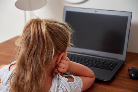 Cute little girl using laptop while sitting at table at homeの写真素材