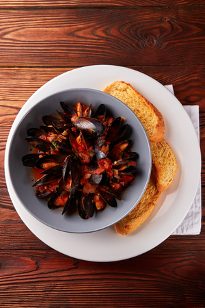 Seafood, mussels with tomato and onion saice in bowl with baguette on wooden tableの写真素材
