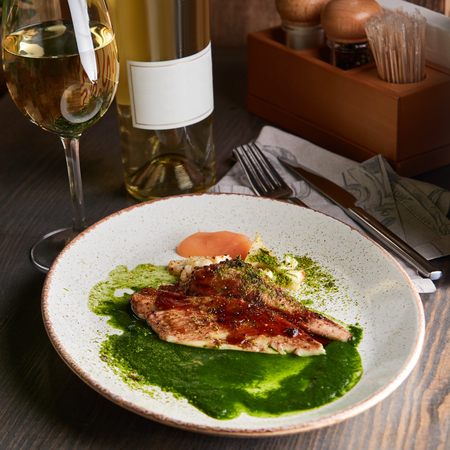 Grilled white fish fillet with roasted cauliflower, spicy green butter and apple sauce, served with wineの写真素材