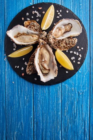 Fine de claire oysters served with lemon slices on blue wooden tableの写真素材