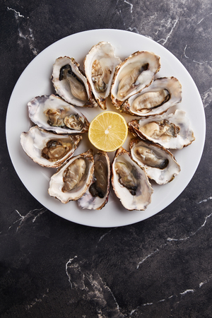 Fresh open oysters served with lemon slices on white plate on black marble tableの写真素材