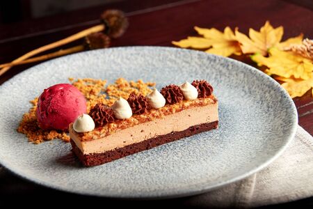 Slice of layered cake with dark chocolate biscuit, milk chocolate mousse, caramelized nuts,...