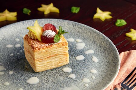 Piece of millefeuille cake decorated with grape, carom and mint leaves on grey plate on wooden background.の写真素材