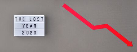 Crisis composition with lightbox with The lost year 2020 slogan and red down arrow on grey paper background. Flat lay top view, minimal style with copy space.の写真素材