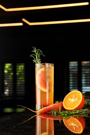 Cocktail with gin, carrot liquor, tonic, orange and rosemary and tonic on black marble bar counterの写真素材