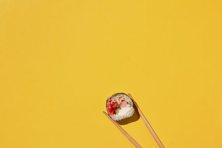 Fresh maki sushi roll with shrimp, eel, salmon, cheese and cucumber and chopsticks on yellow background, top view.の写真素材