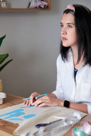 Creative young adult woman making sewing patterns for handmade doll, drawing on cloth.の写真素材